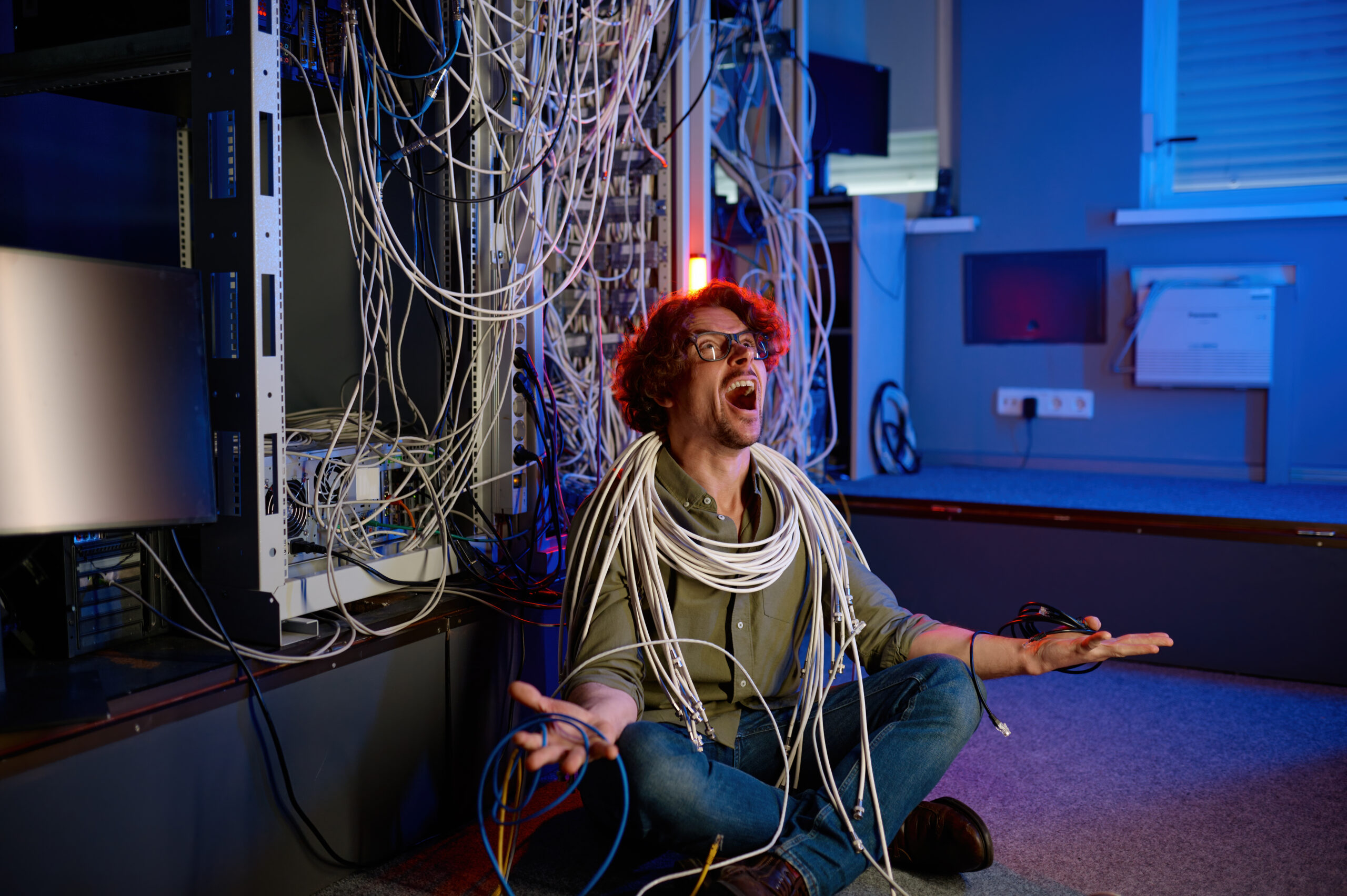 Frustrated IT technician sitting on the floor tangled in network cables, symbolizing tool sprawl and technology overload in MSPs