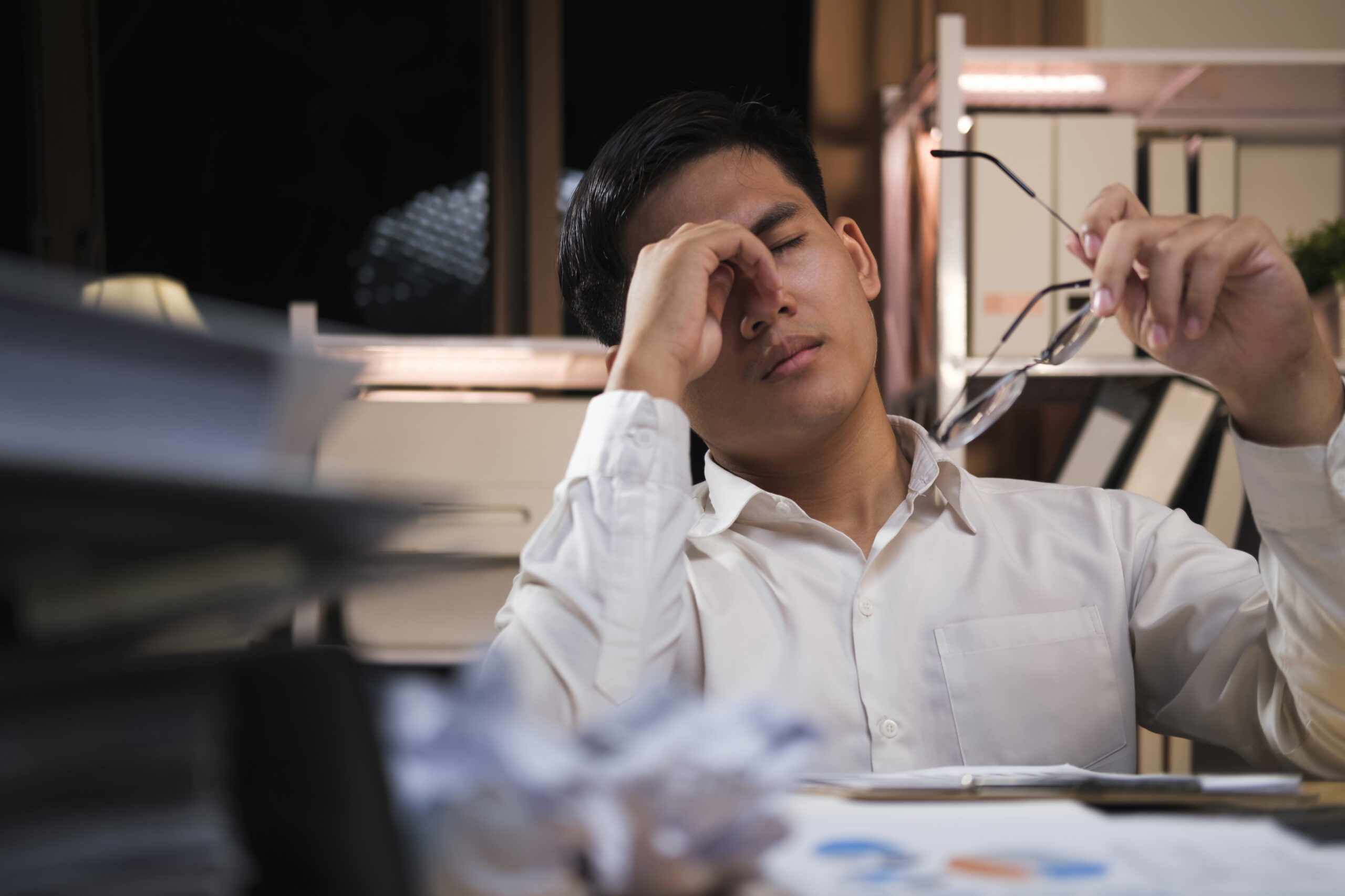 IT professional showing signs of MSP burnout while working late at the office surrounded by paperwork.